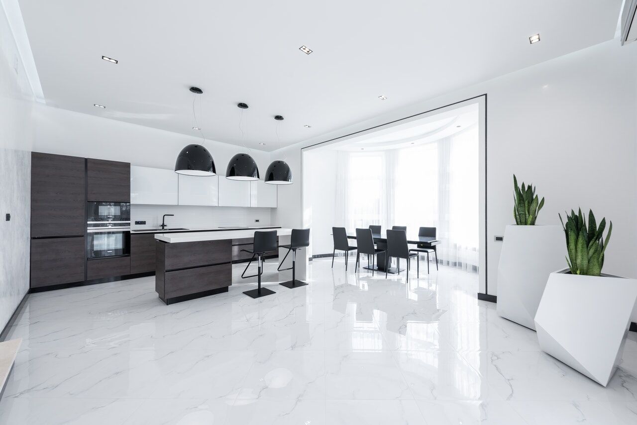Spacious modern kitchen with white marble flooring, dark cabinets, and a dining area with black chairs