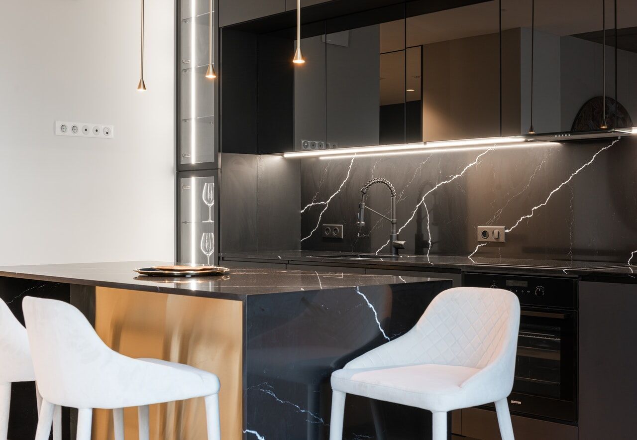 Modern kitchen with black marble countertop and backsplash, white chairs at the island