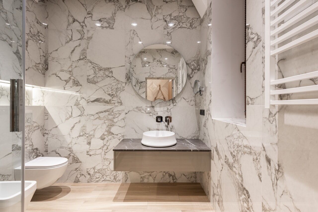 Modern bathroom with white marble walls, floating vanity, and round mirror