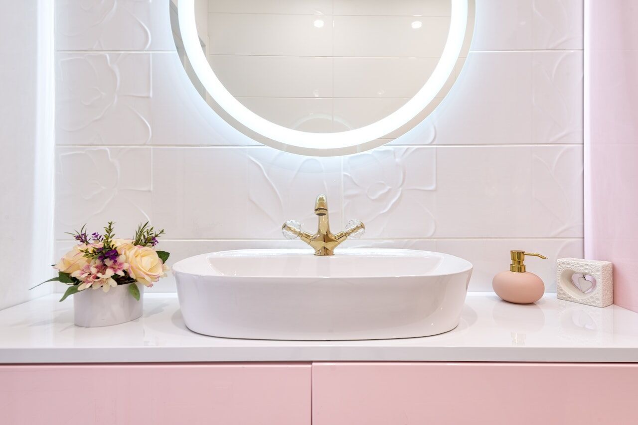 Modern bathroom sink with round illuminated mirror, floral decor, and soap dispenser on white countertop