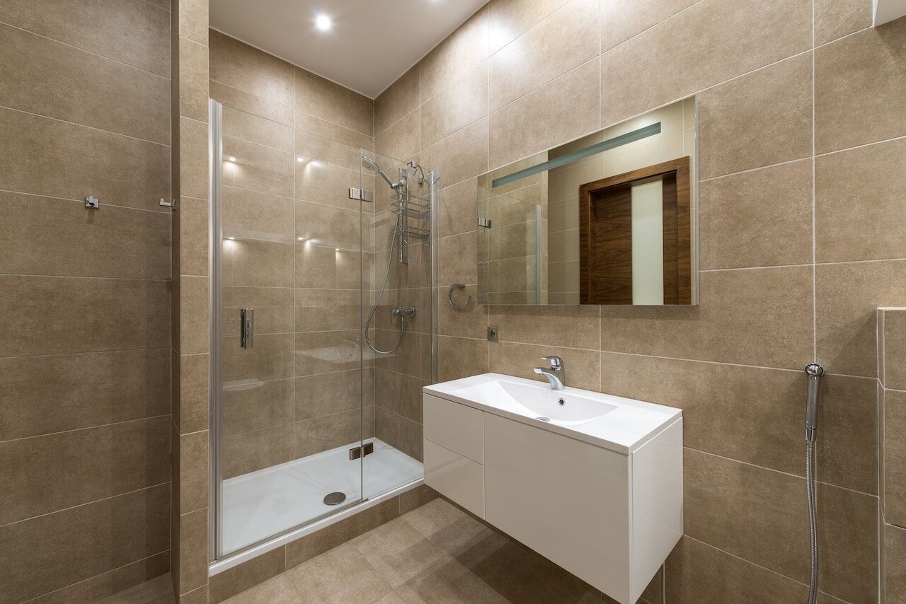 Modern bathroom with beige tiles, glass shower, and white vanity with mirror