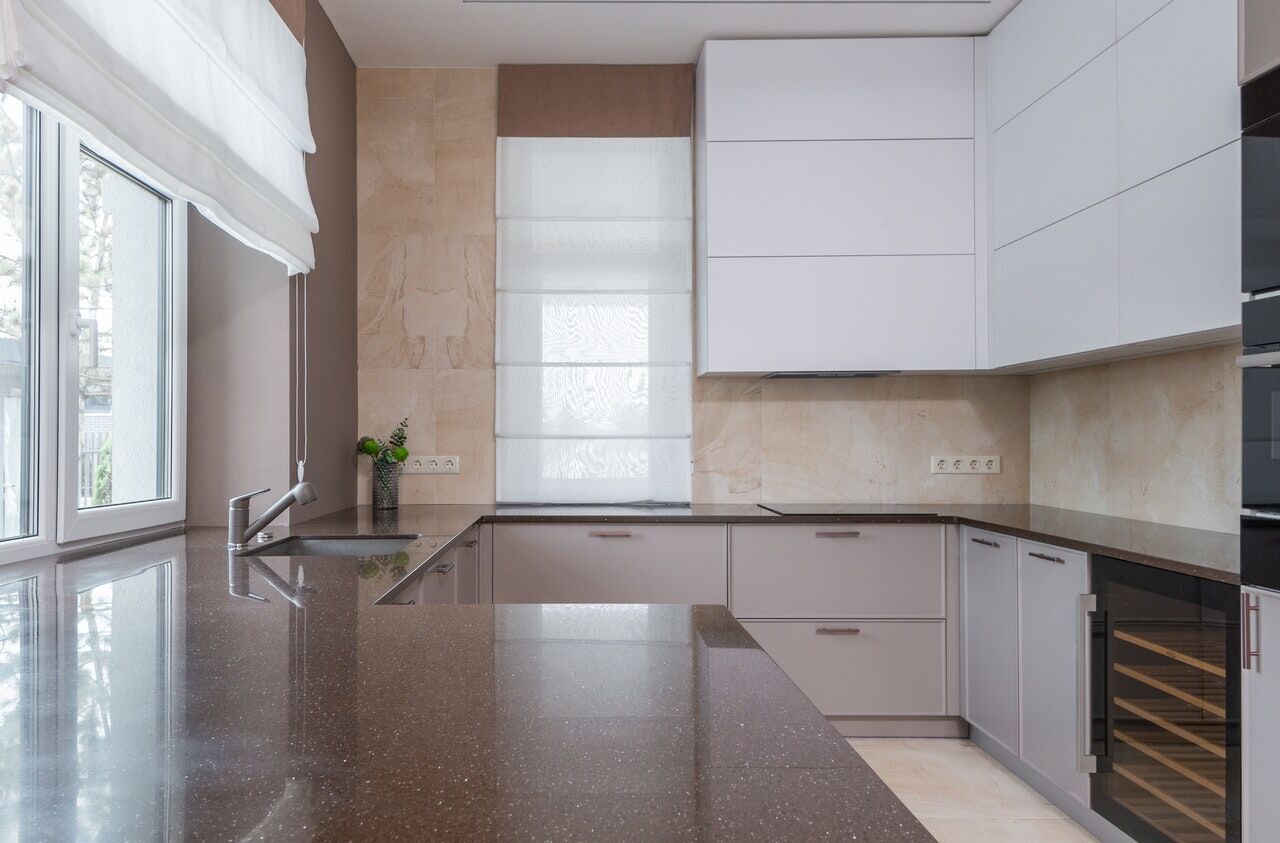 Modern kitchen featuring a dark quartz countertop, white cabinets, and a wine cooler under natural light