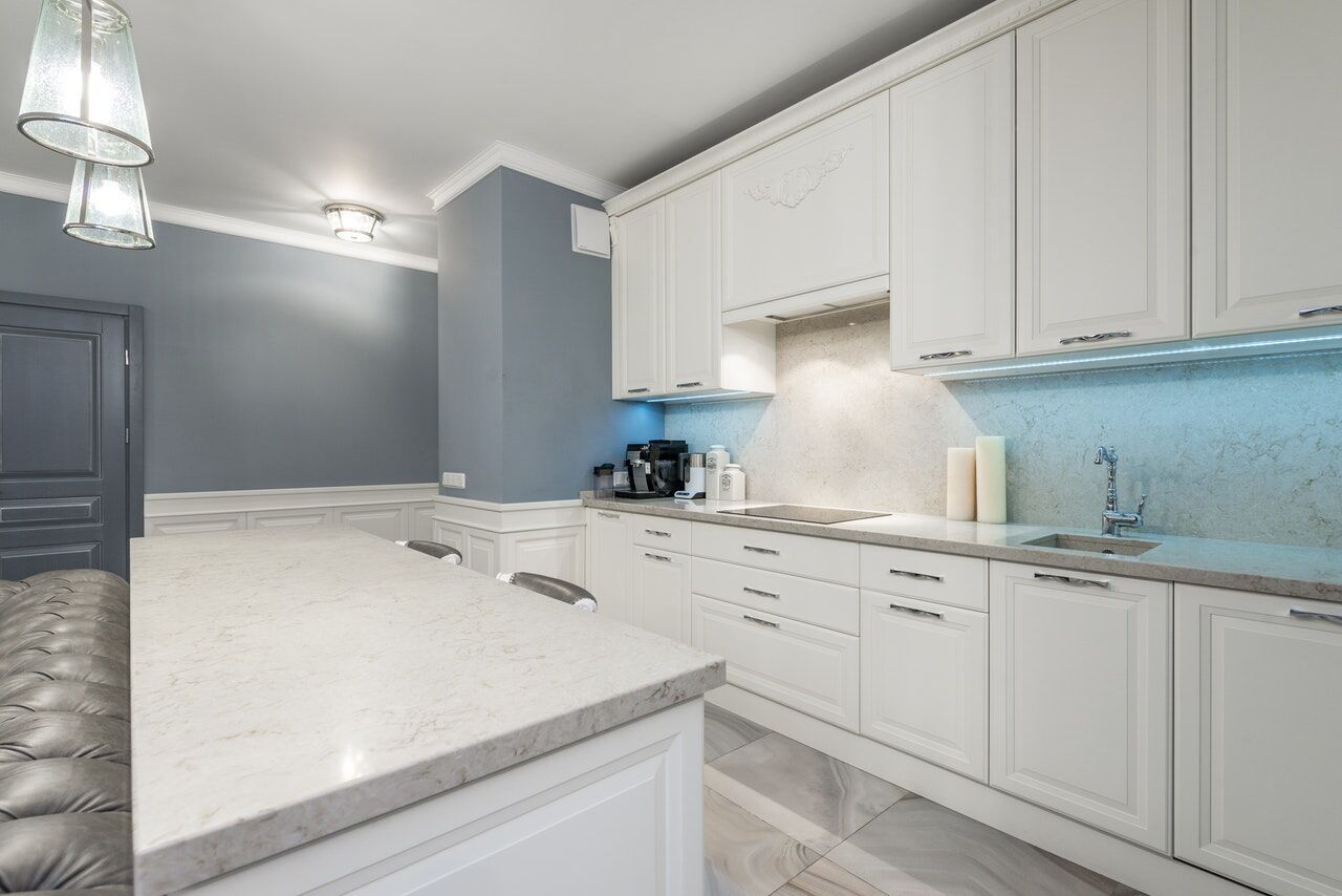 Modern kitchen with a large quartz countertop island, white cabinets, and stainless steel fixtures