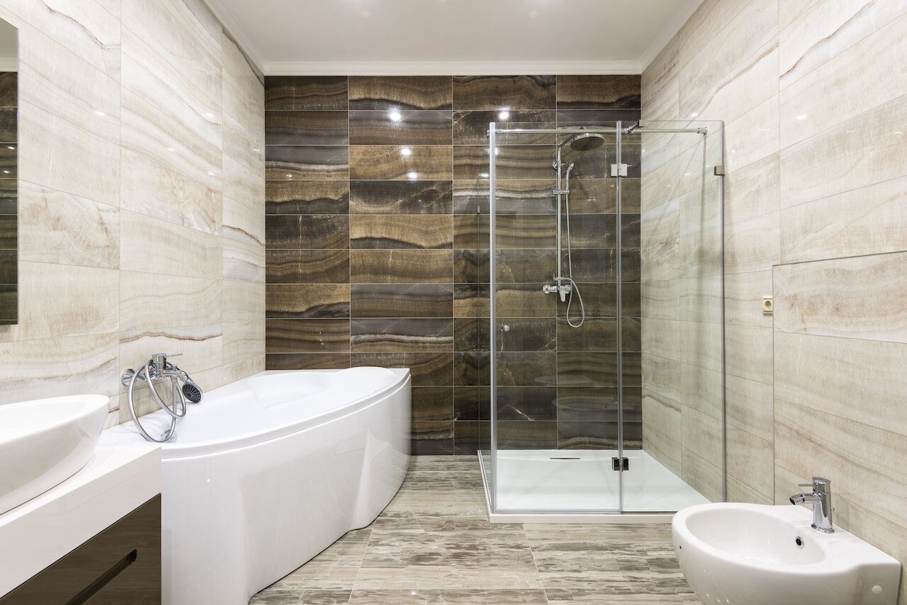 Modern bathroom with glass shower, freestanding tub, and beige-brown tiles