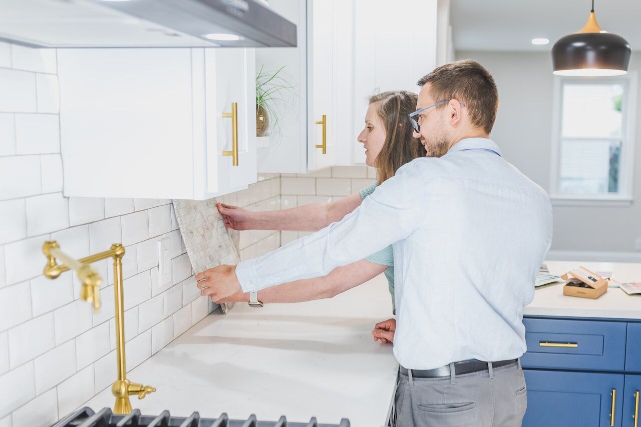 Man and woman examining tile sample in kitchen with white subway tiles and gold fixtures