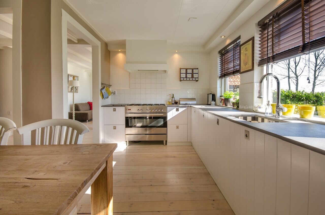 Bright kitchen with wooden floors, white cabinets, and large window with blinds