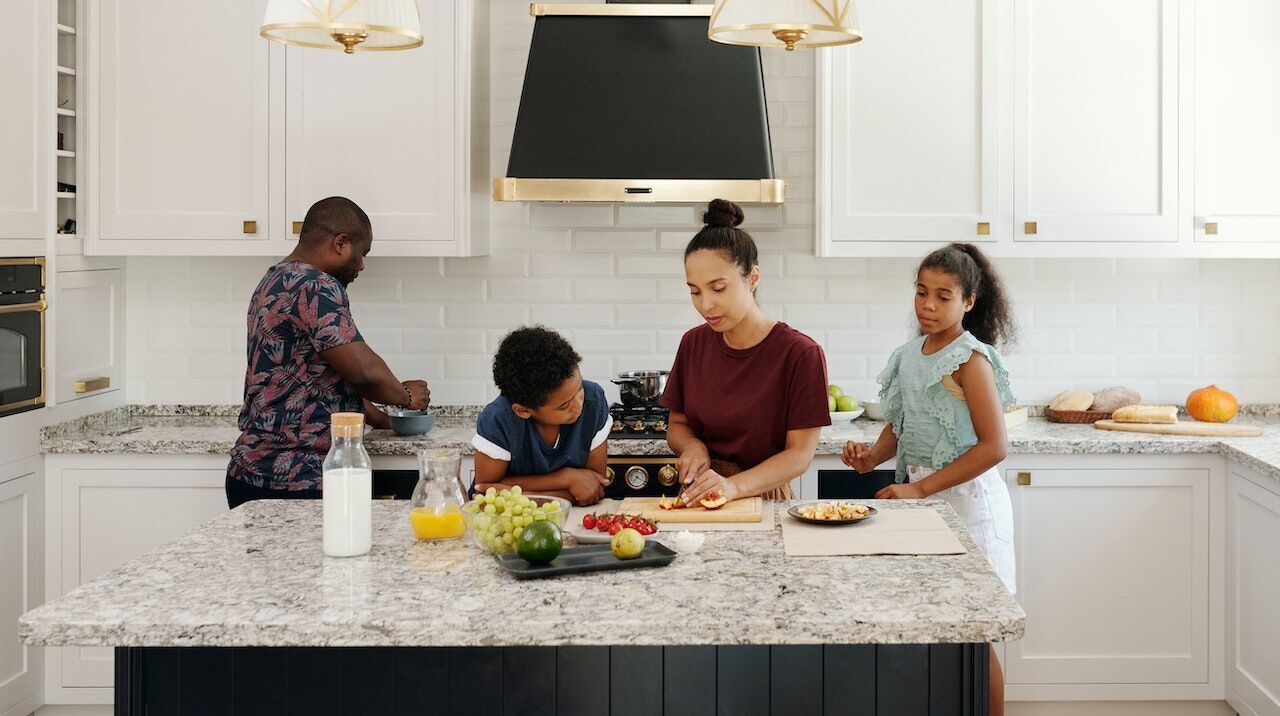 Family preparing food in a kitchen with a granite countertop and white cabinets