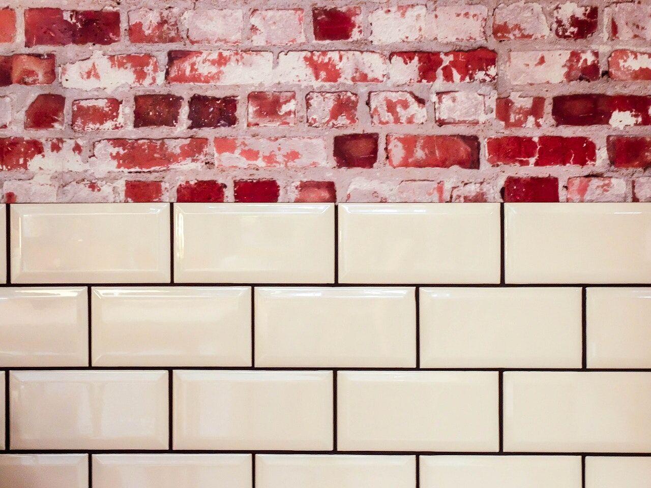 Cream subway tiles on a wall with exposed red brick above