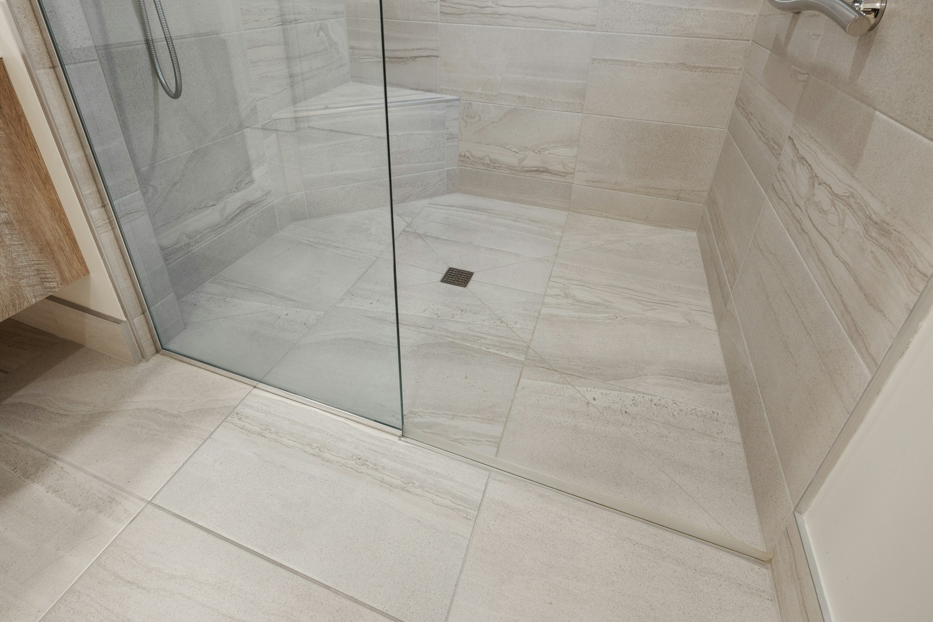 Shower area with large-format beige tiles, glass door, and metal drain