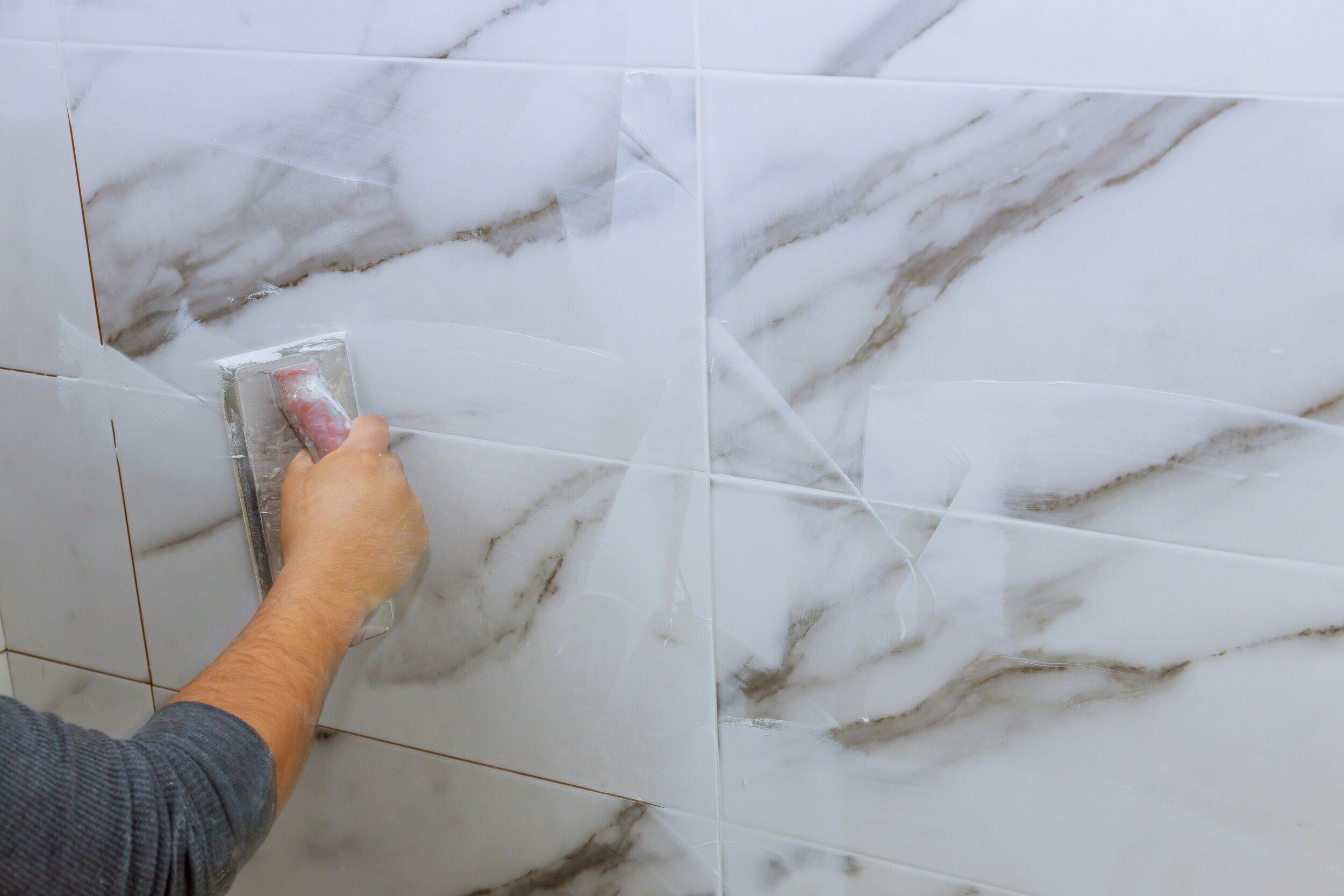Hand applying grout to seams between marble-like tiles with a rubber float