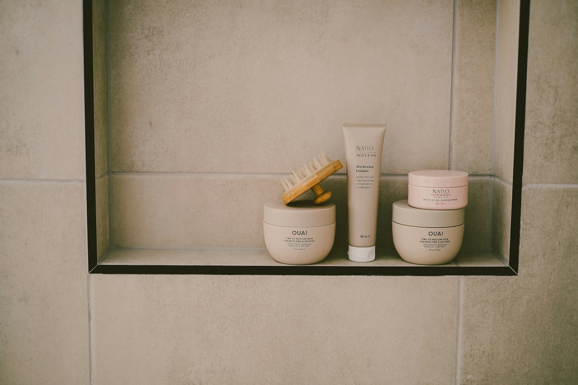 Shower niche with beige tiles containing skincare products and a brush