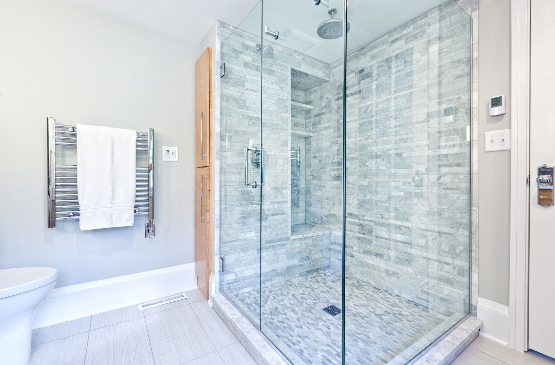 Modern shower with glass doors and gray stone tile walls and floor, featuring a towel rack