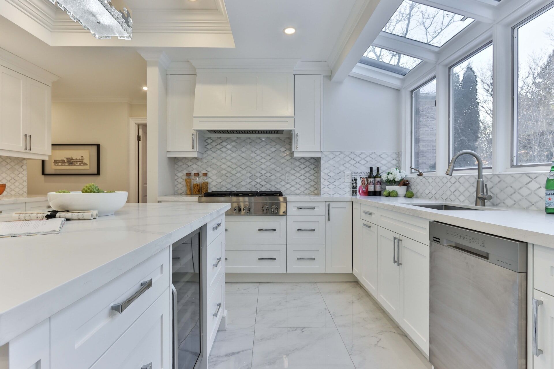 Modern kitchen featuring white cabinets, marble countertops, and a tile backsplash with large windows