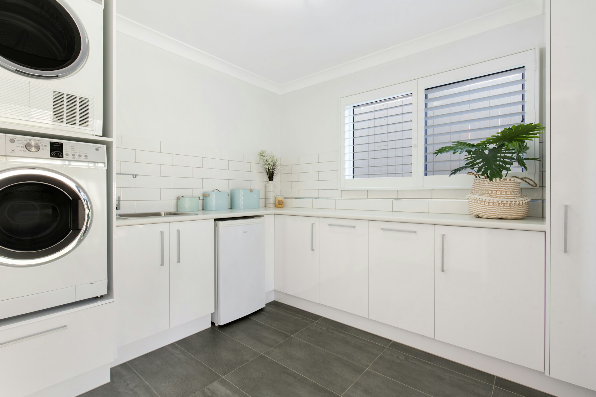 Laundry room featuring white cabinets, stacked washer and dryer, and subway tile backsplash