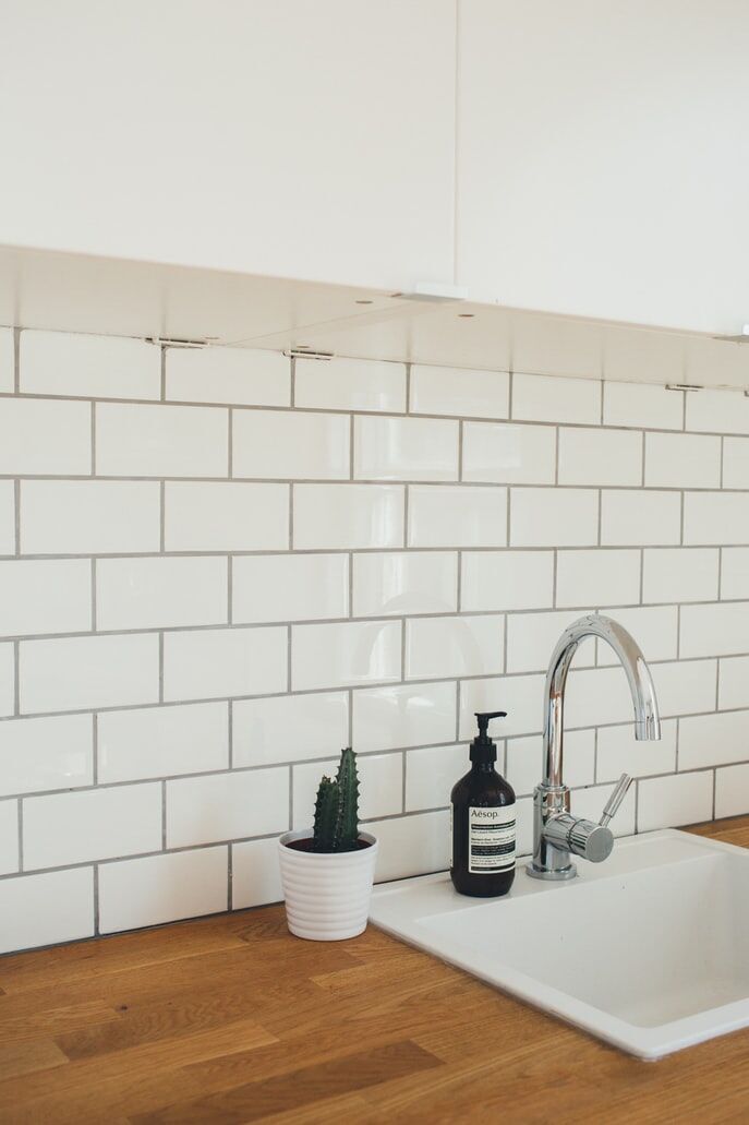 White subway tile backsplash with chrome faucet, white sink, wooden countertop, cactus, and soap dispenser