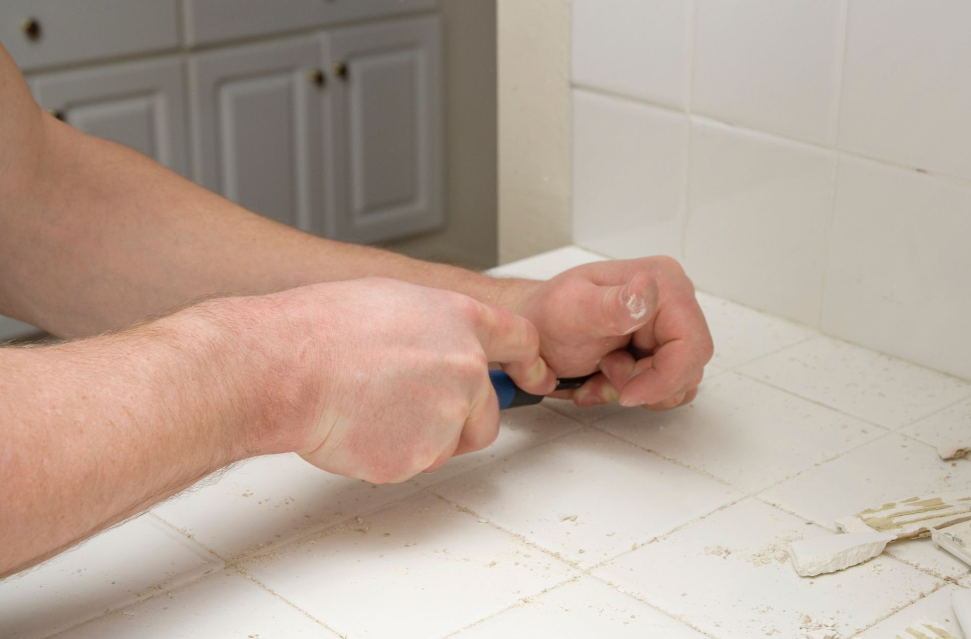 Person removing grout from white ceramic tiles using a tool