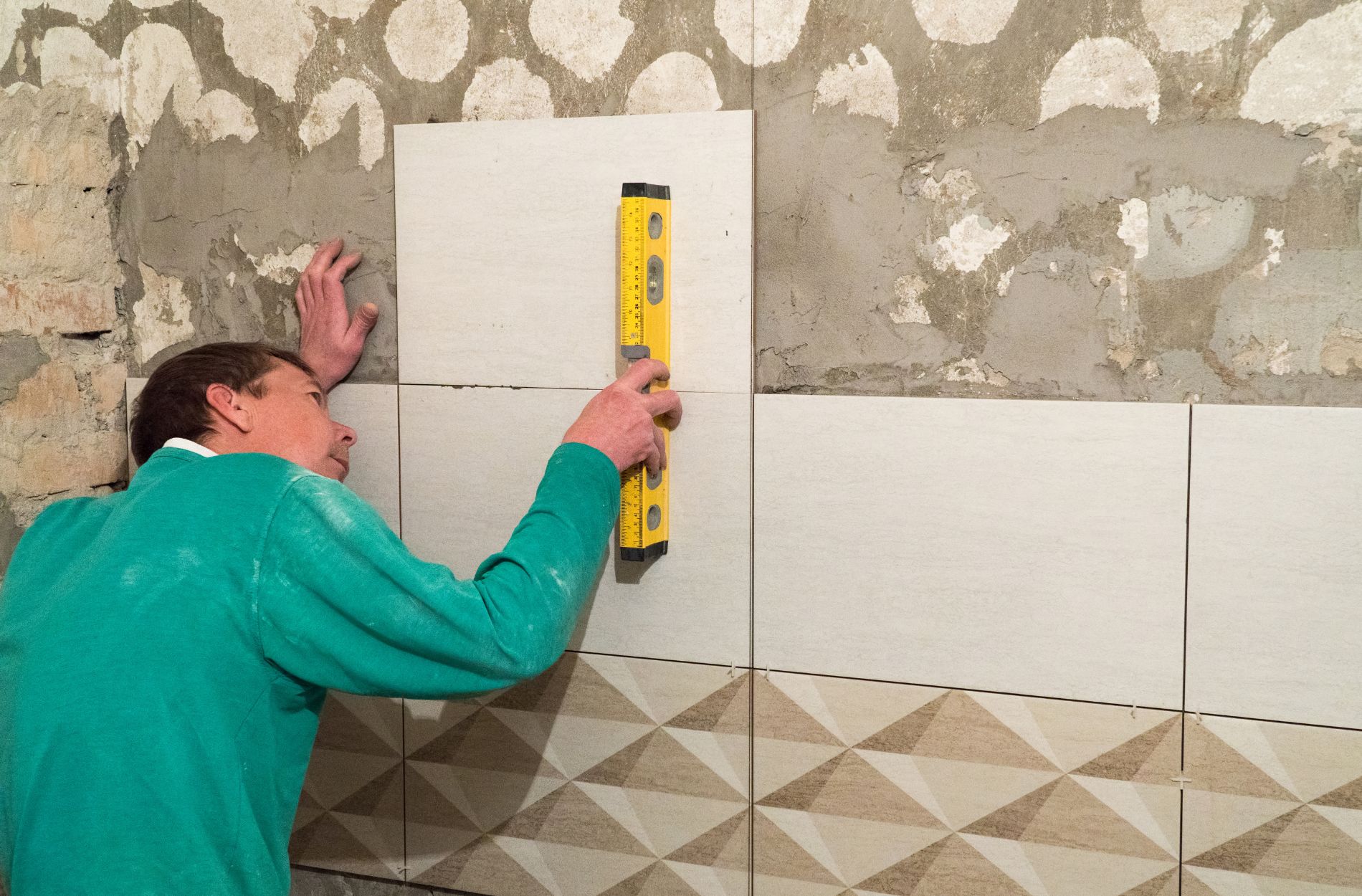 Person using a level to install tiles on a wall, ensuring proper alignment and pattern consistency