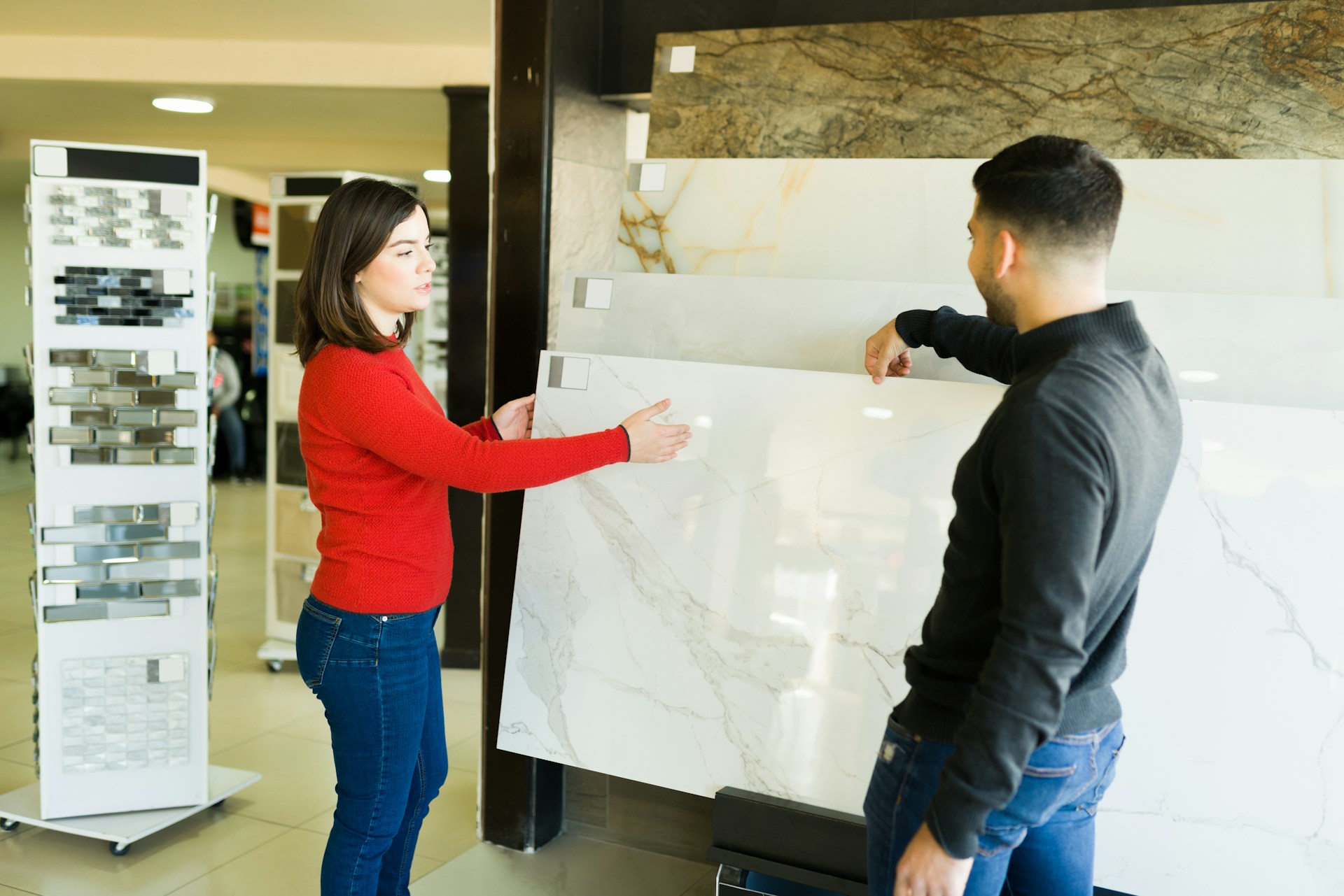 Two people looking at marble slabs in a tile store showroom with tile samples in the background
