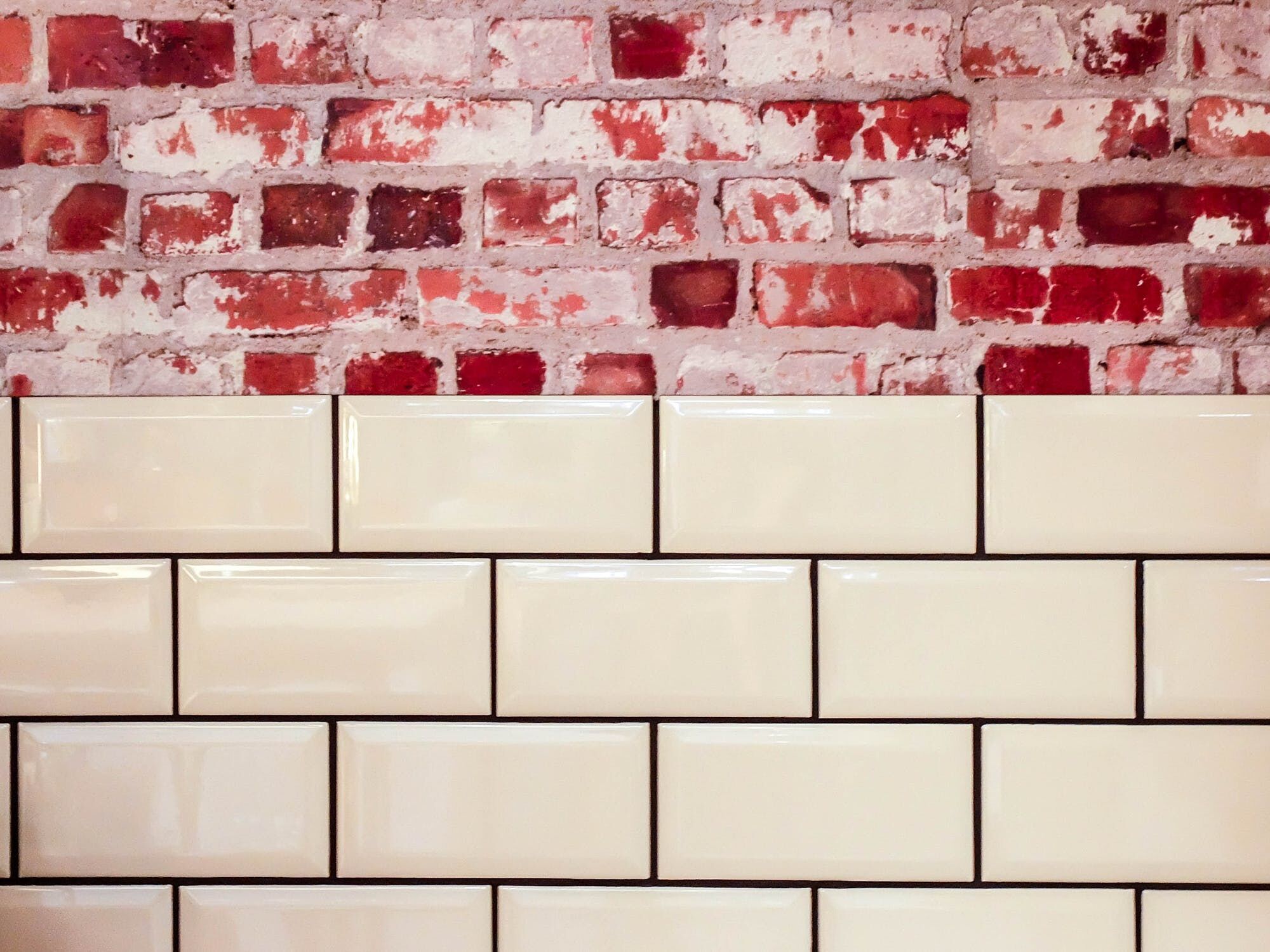Cream subway tiles with a red brick wall above, showcasing tile installation contrast