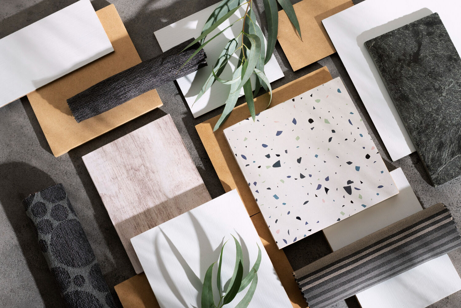 Top view of material samples including terrazzo, wood, and stone with decorative leaves