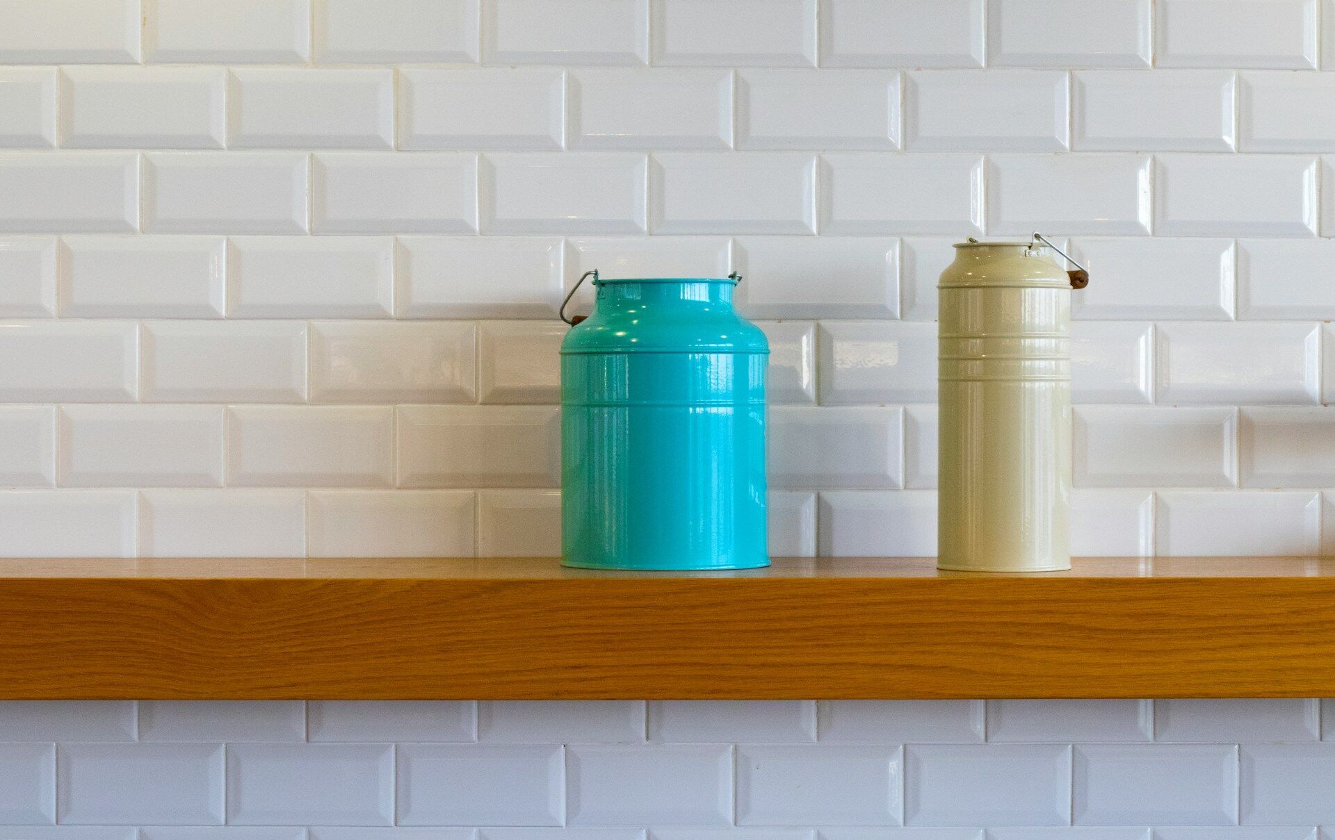 White subway tile wall with a wooden shelf and two metal canisters, one blue and one beige